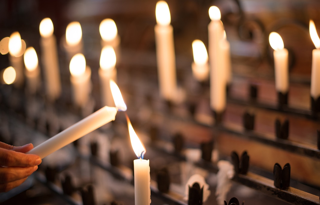 Woman lighting a candle in a dimly lit setting with multiple candles in the background.