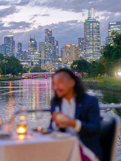 Couple dining on a Spirit of Melbourne Dinner Cruise with city skyline in the background.
