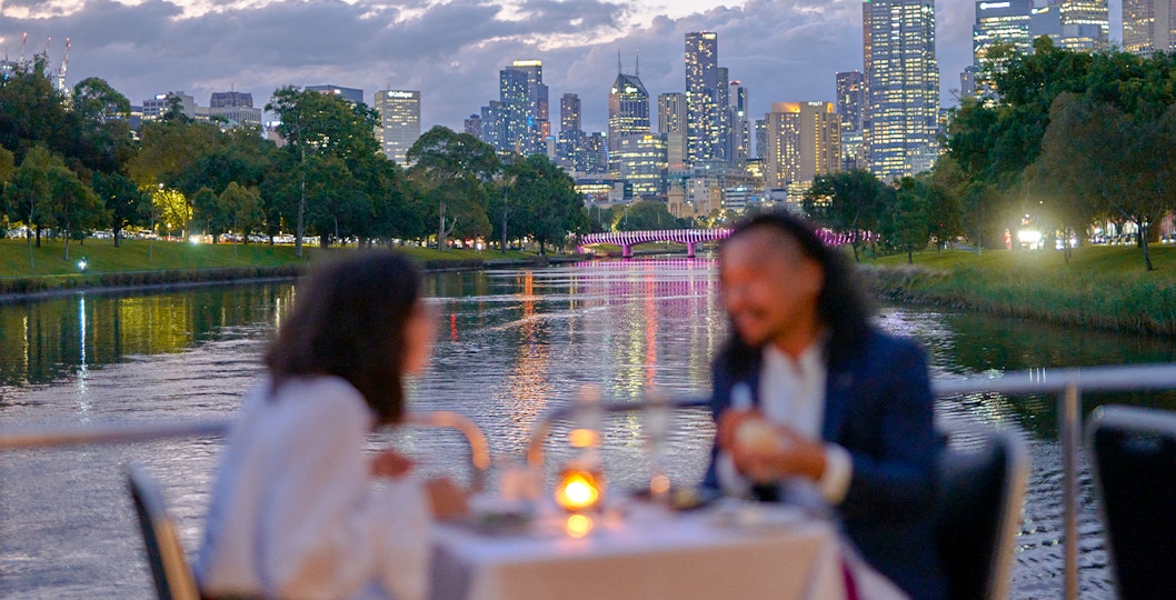 Couple dining on a Spirit of Melbourne Dinner Cruise with city skyline in the background.