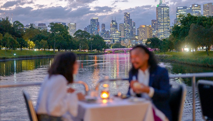 Couple dining on a Spirit of Melbourne Dinner Cruise with city skyline in the background.