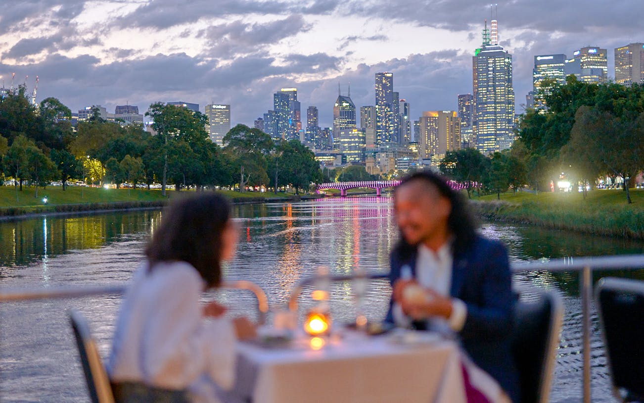 Couple dining on a Spirit of Melbourne Dinner Cruise with city skyline in the background.