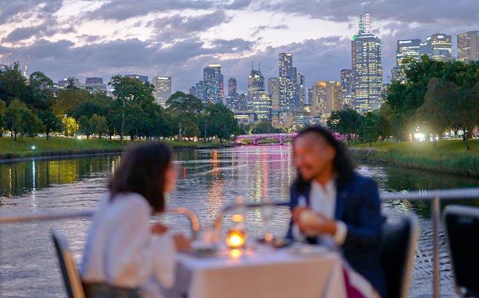 Couple dining on a Spirit of Melbourne Dinner Cruise with city skyline in the background.