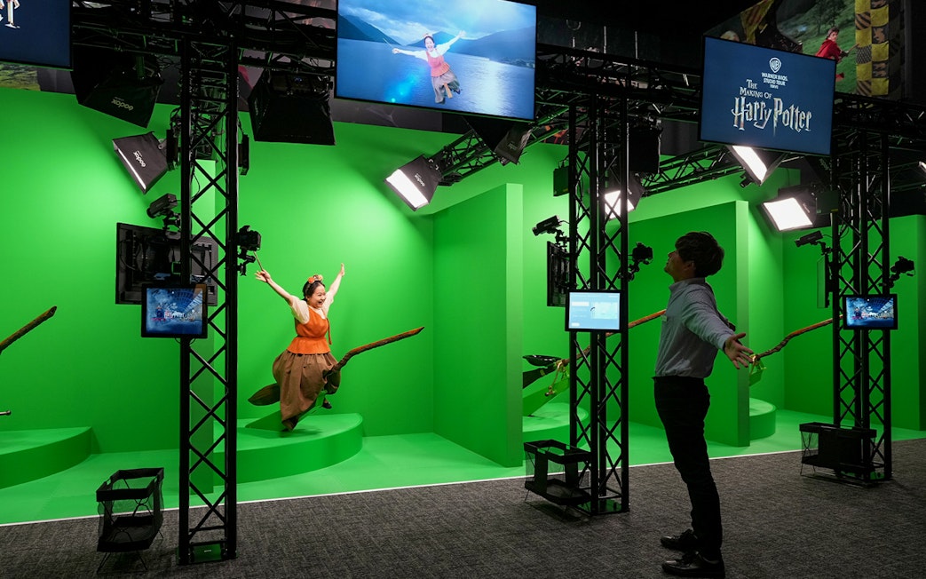 Quidditch simulation at Warner Bros. Studio Tour Tokyo with visitors on broomsticks against green screen.