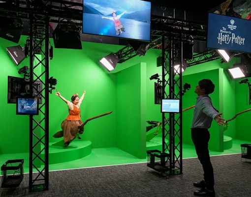 Quidditch simulation at Warner Bros. Studio Tour Tokyo with visitors on broomsticks against green screen.