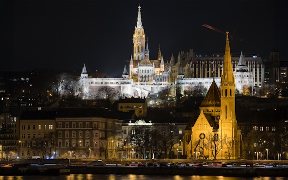 Fisherman's Bastion illuminated at night, viewed from a Danube River cruise in Budapest.