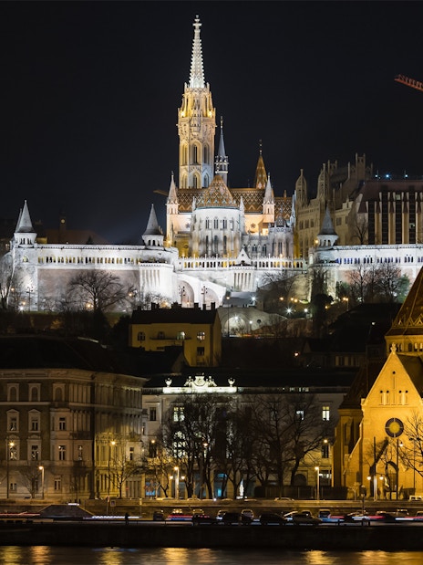 Fisherman's Bastion illuminated at night, viewed from a Danube River cruise in Budapest.