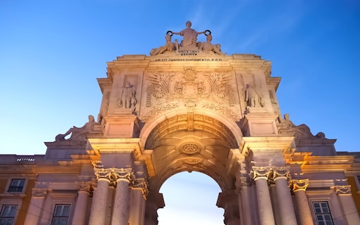 Arco da Rua Augusta in Lisbon at sunset, showcasing detailed sculptures and architecture.