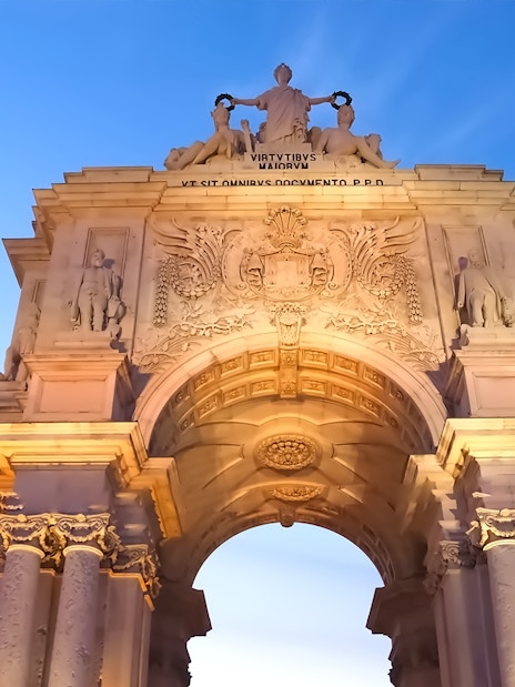 Arco da Rua Augusta in Lisbon at sunset, showcasing detailed sculptures and architecture.