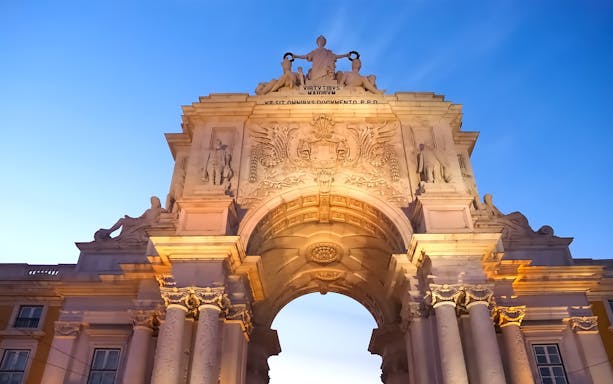 Arco da Rua Augusta in Lisbon at sunset, showcasing detailed sculptures and architecture.