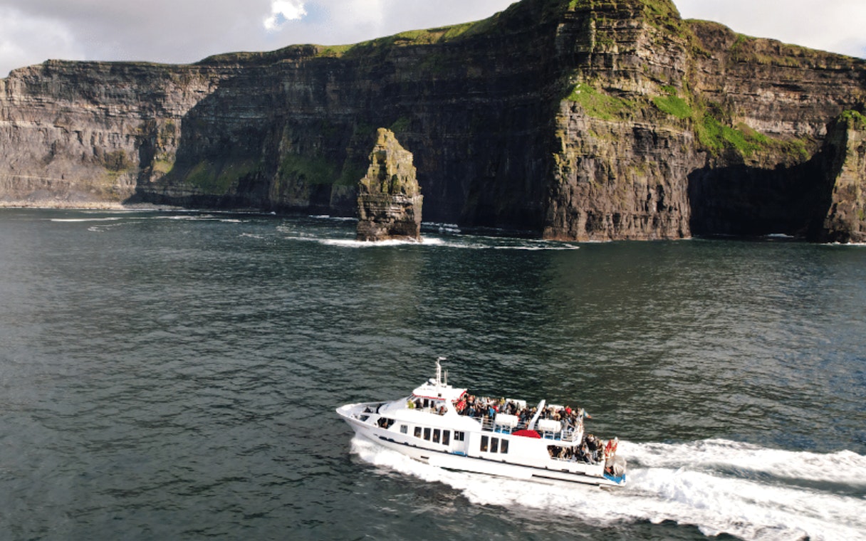 Boat tour approaching the Cliffs of Moher, Ireland, with passengers viewing the scenic cliffs.