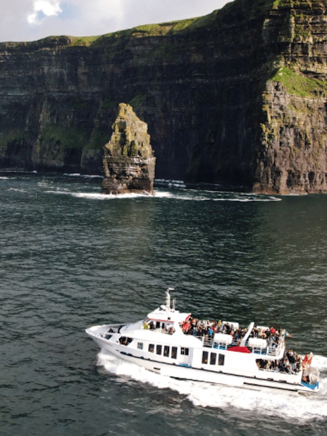 Boat tour approaching the Cliffs of Moher, Ireland, with passengers viewing the scenic cliffs.