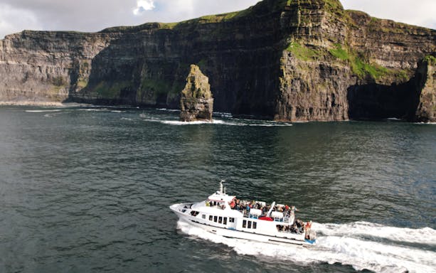 Aerial view of a boat approaching the Cliffs of Moher, Ireland, showcasing the rugged coastline and Atlantic Ocean.