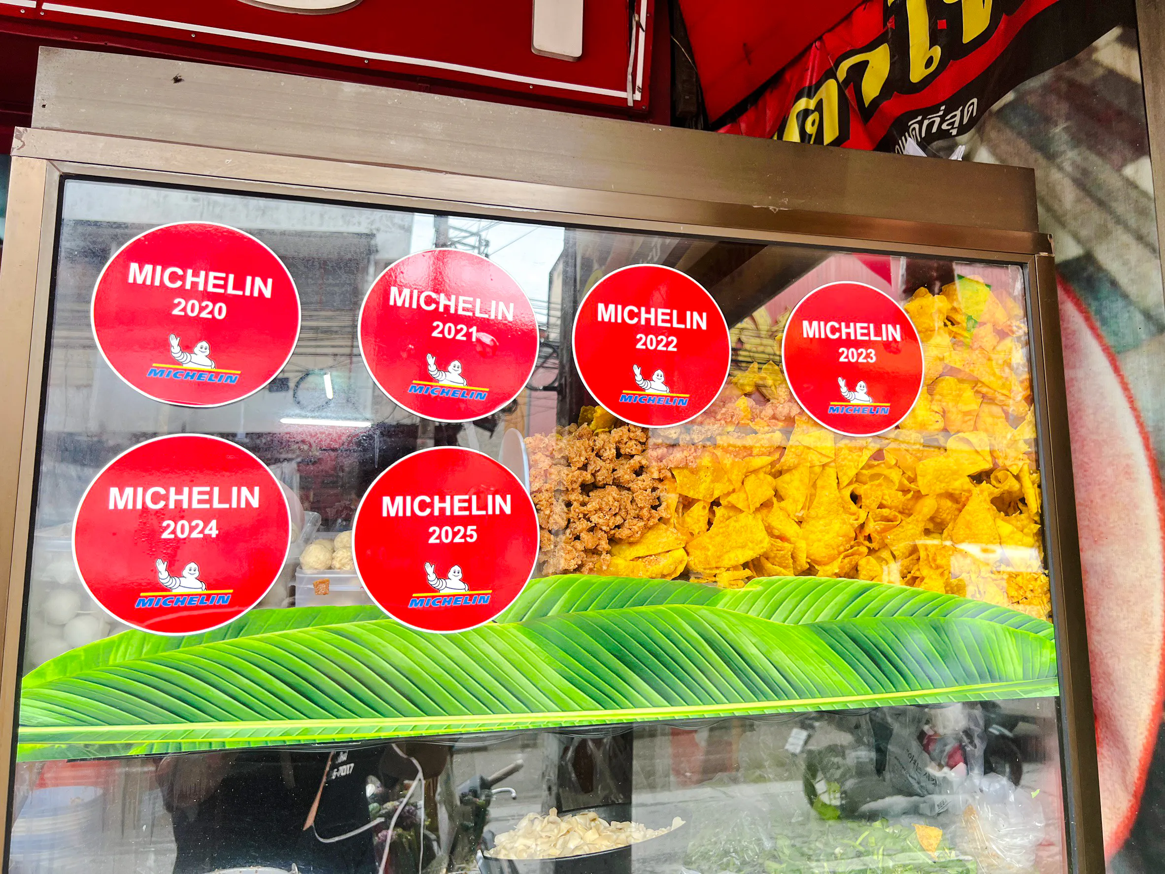 Michelin stickers on a food stall window in Chiang Mai, showcasing local snacks.