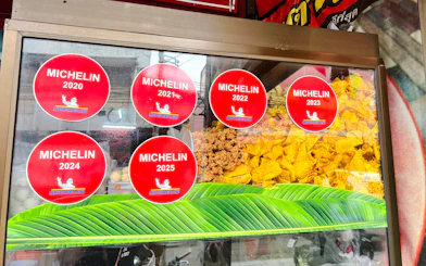 Michelin stickers on a food stall window in Chiang Mai, showcasing local snacks.