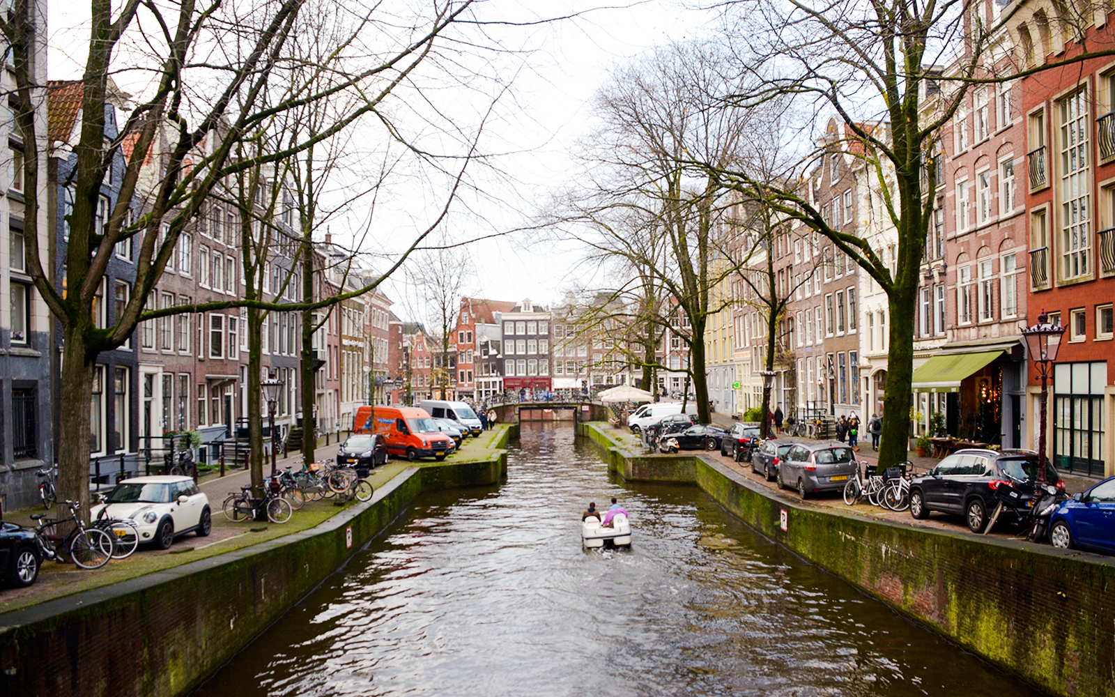 Paddle boat on Amsterdam canal with historic buildings and bridge.