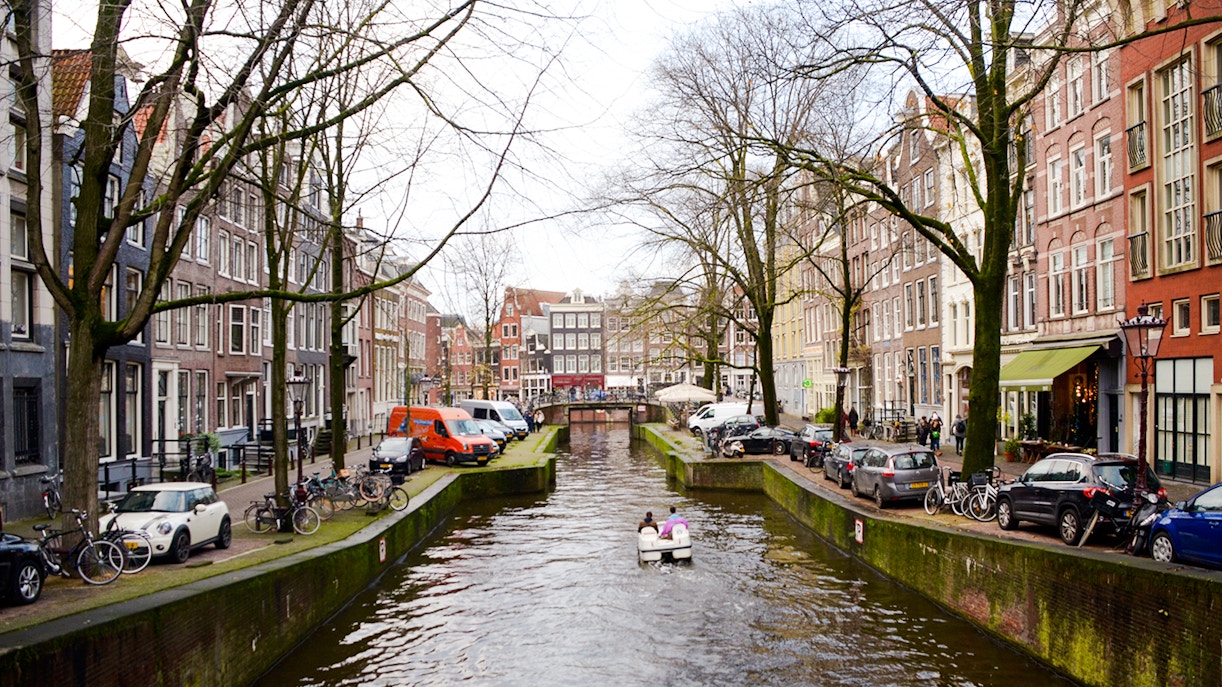 Paddle boat on Amsterdam canal with historic buildings and bridge.