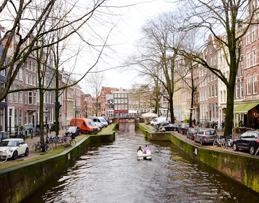 Paddle boat on Amsterdam canal with historic buildings and bridge.