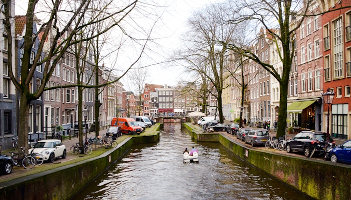 Paddle boat on Amsterdam canal with historic buildings and bridge.