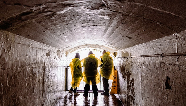 Visitors exploring Niagara Underground Tailrace Tunnel with view of historic brick walls.