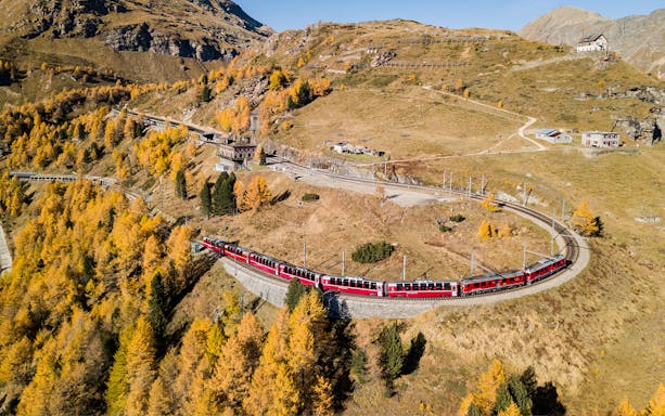 Bernina Express train winding through autumnal Swiss Alps en route to St. Moritz from Milan.