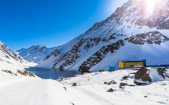 Yellow and blue Hotel Portillo in snowy Andes mountains, Chile, near a serene lake.