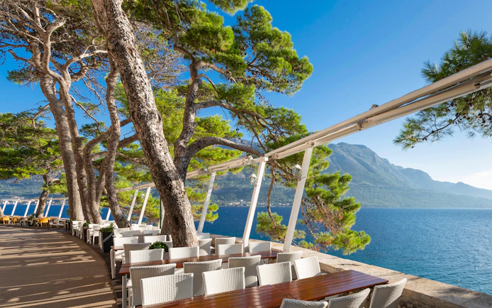 Empty restaurant terraces with tables and chairs along Korčula's city wall, overlooking the sea, Croatia.