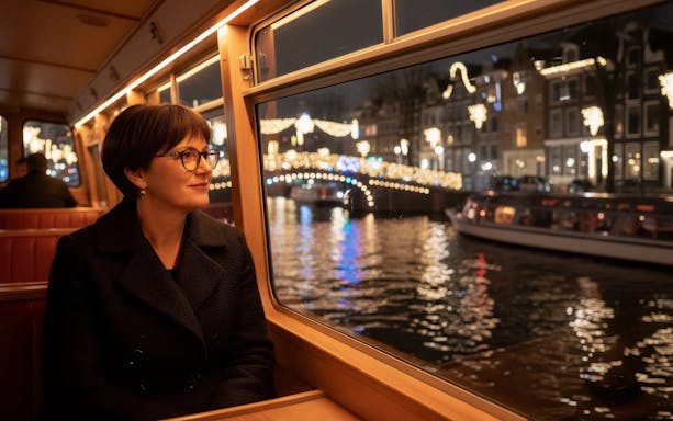Person enjoying Amsterdam Light Festival canal cruise with illuminated bridge view.