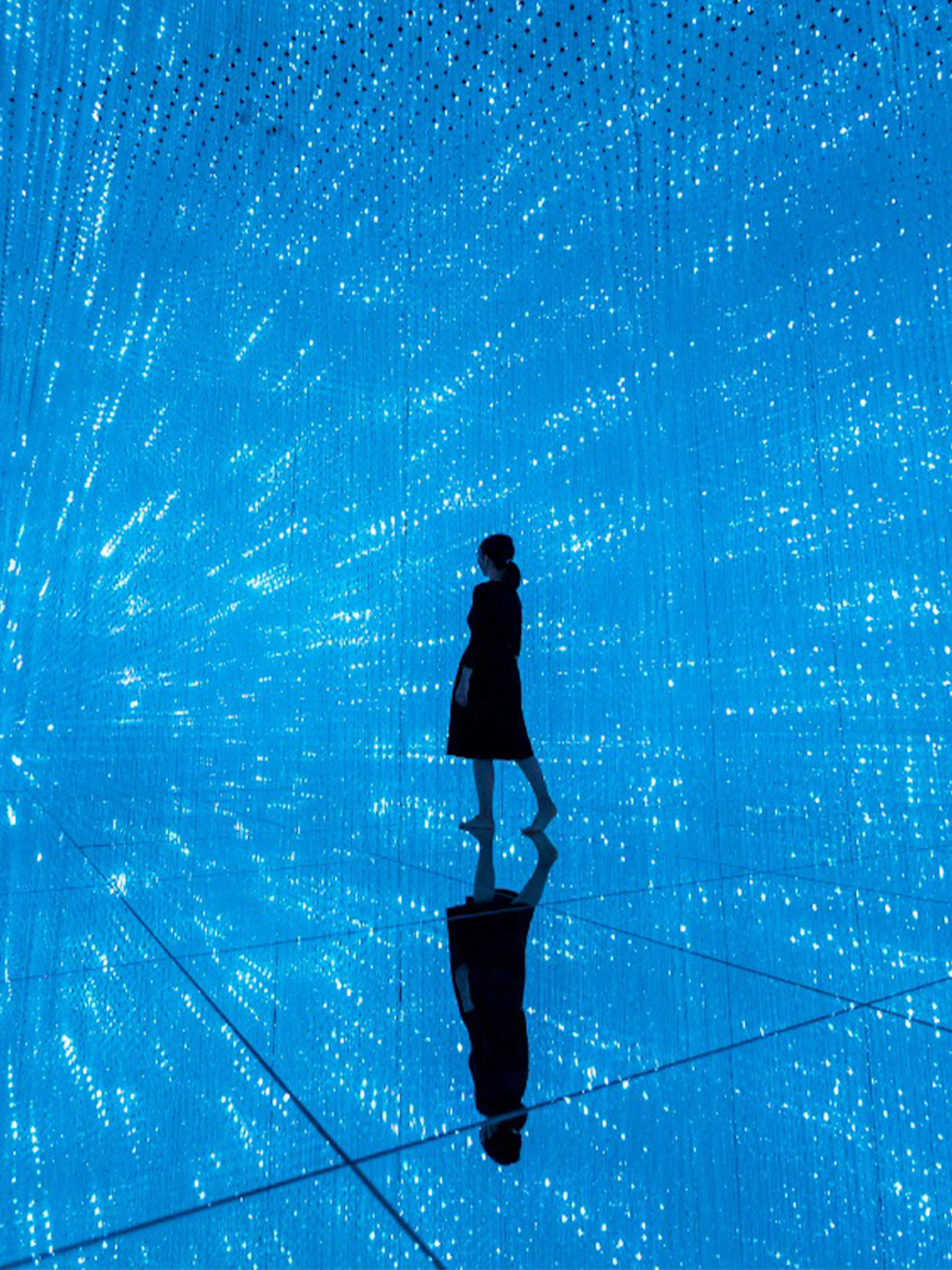 Person walking through digital light installation at TeamLab Planets Tokyo exhibit.