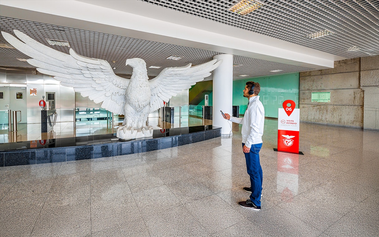 Man observing large eagle statue in Benfica Stadium's eagle hall, Lisbon.