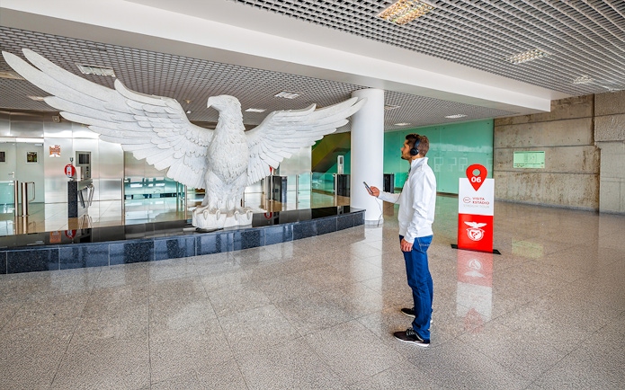 Man observing large eagle statue in Benfica Stadium's eagle hall, Lisbon.