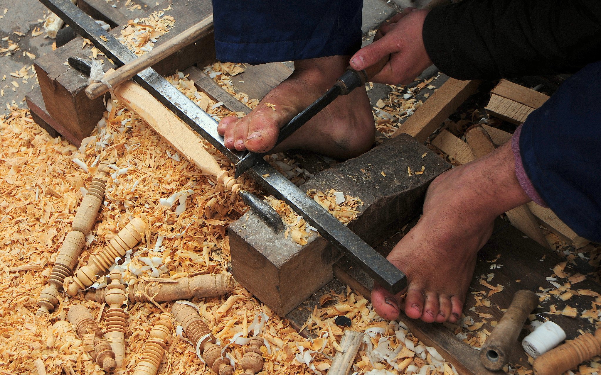 Woodworker carving with feet in Marrakech souk near Ben Youssef Medersa.