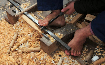 Woodworker carving with feet in Marrakech souk near Ben Youssef Medersa.