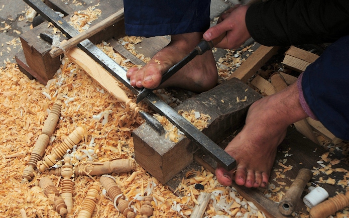 Woodworker carving with feet in Marrakech souk near Ben Youssef Medersa.