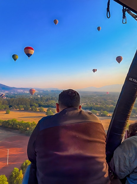 Passengers in a hot air balloon over Teotihuacan with distant balloons and landscape.