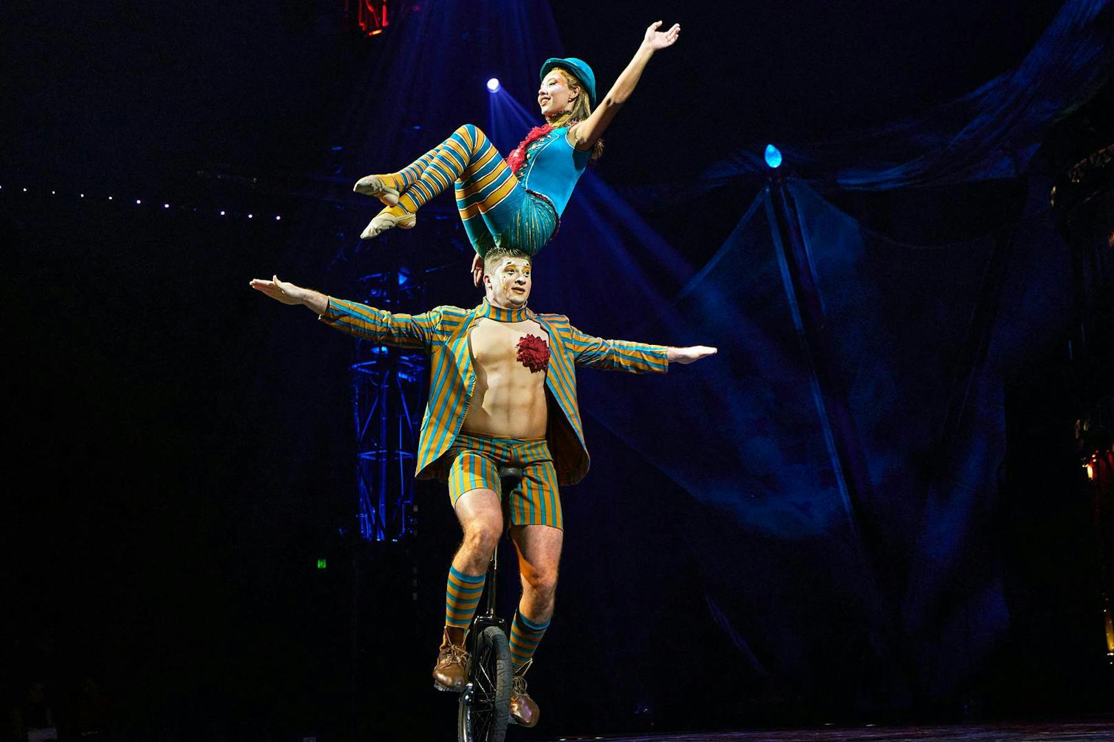 Performer balancing on unicycle with acrobat on shoulders during Kooza stage show.