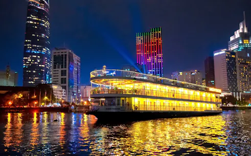 Cruise ship illuminated at night on Saigon River with city skyline in the background.