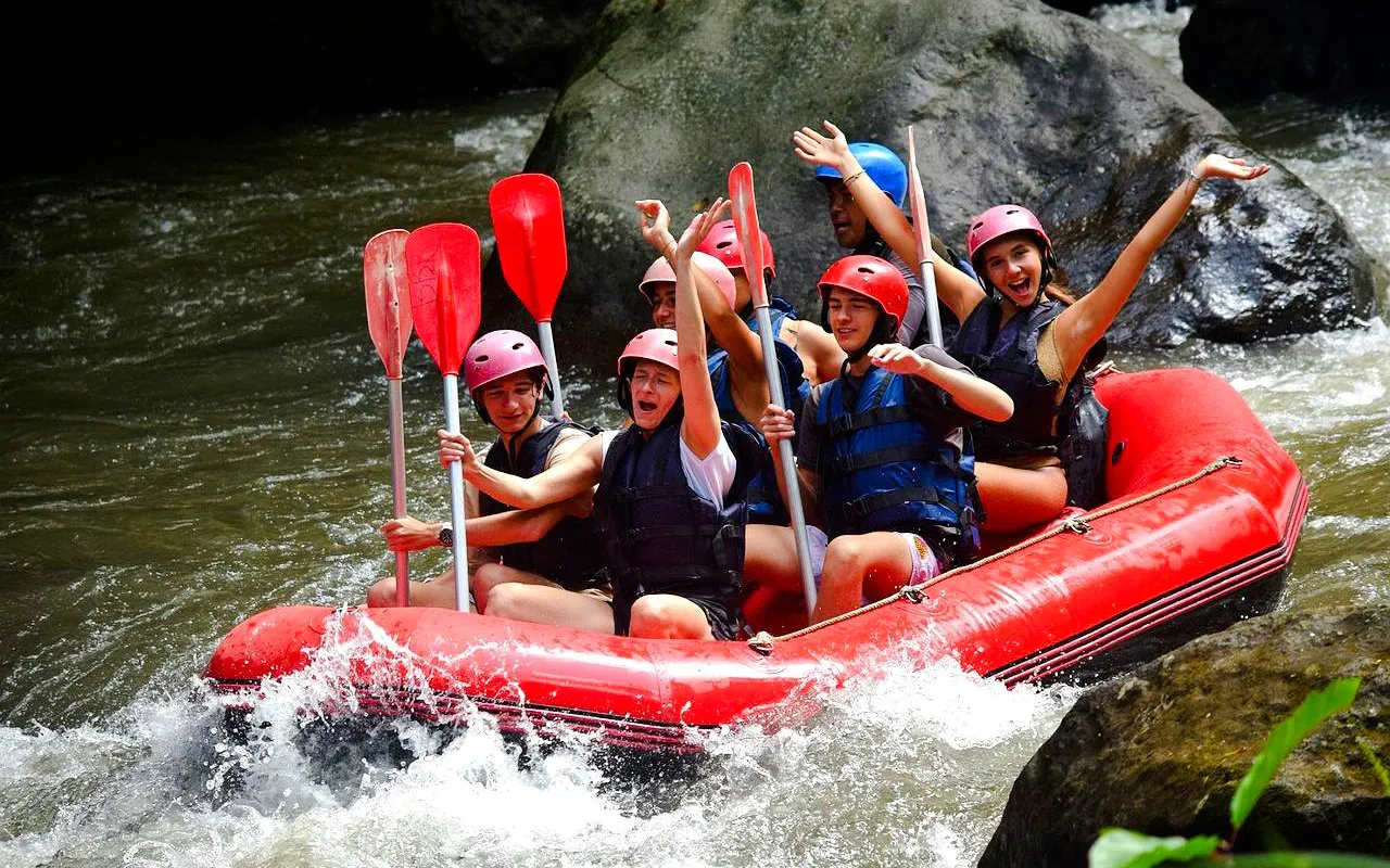 Group rafting on Ayung River in red inflatable boat, wearing helmets and life vests.