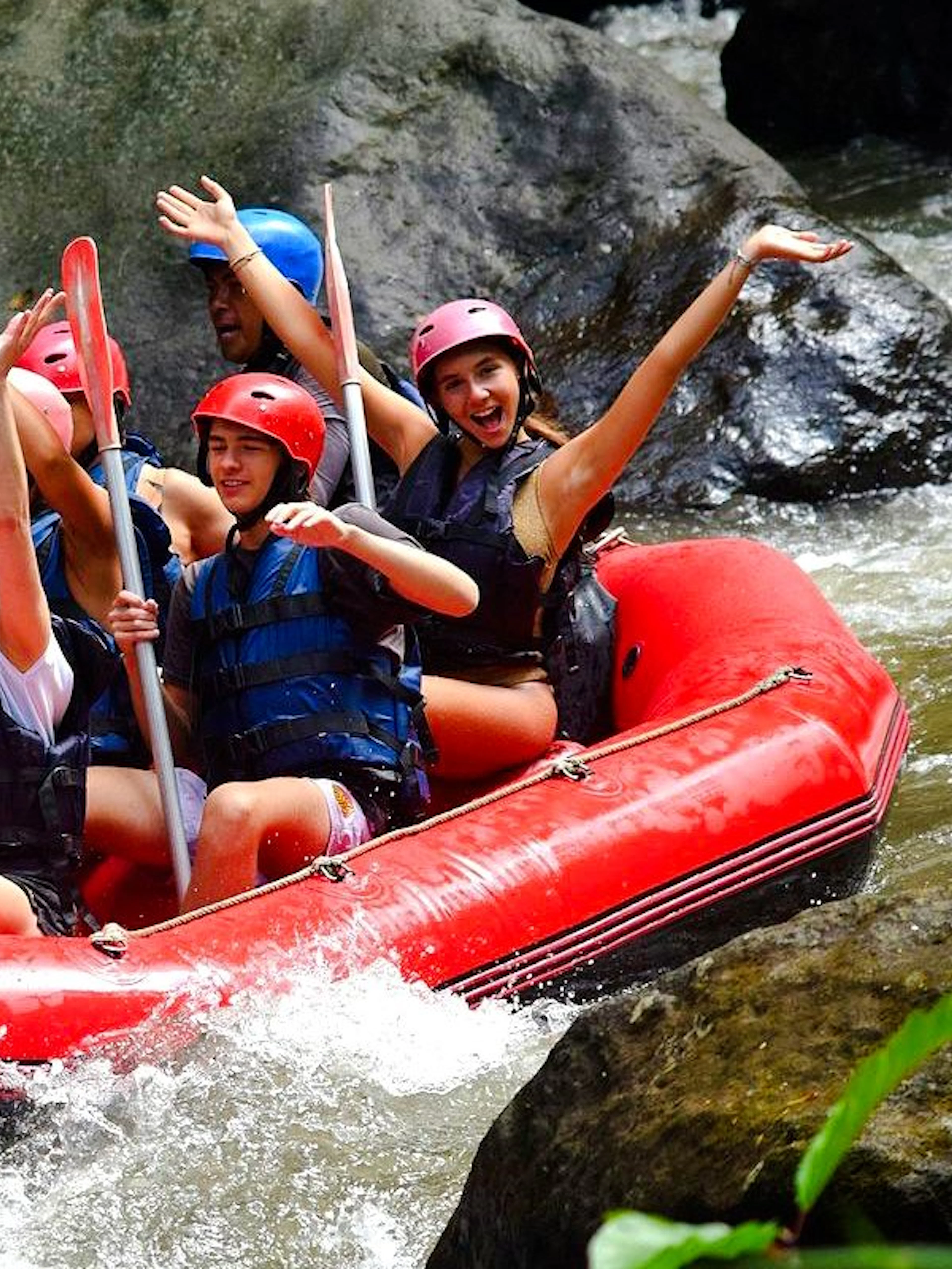 Group rafting on Ayung River in red inflatable boat, wearing helmets and life vests.