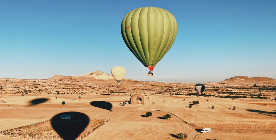 Green hot air balloon floating over desert landscape near Marrakech.