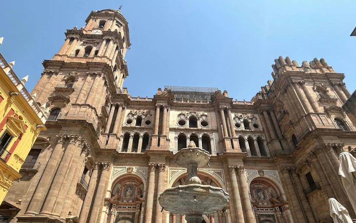Málaga Cathedral facade with ornate architecture and central fountain under a clear sky.