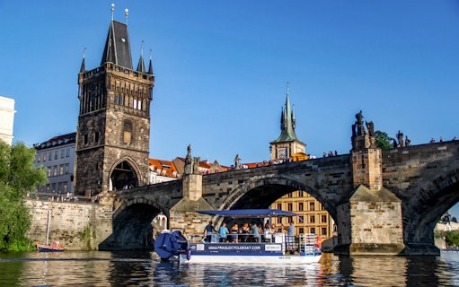 Cycle boat on Vltava River near Charles Bridge, Prague, with tourists enjoying unlimited beer.