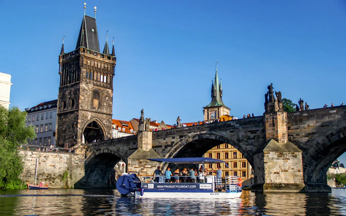 Cycle boat on Vltava River near Charles Bridge, Prague, with tourists enjoying unlimited beer.
