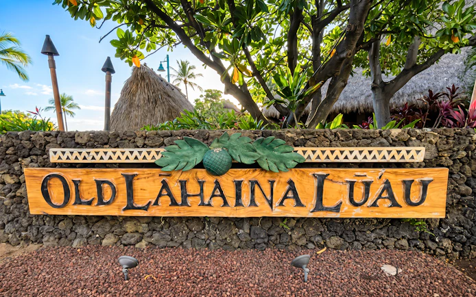 Old Lahaina Luau entrance sign with tropical foliage in Maui, Hawaii.