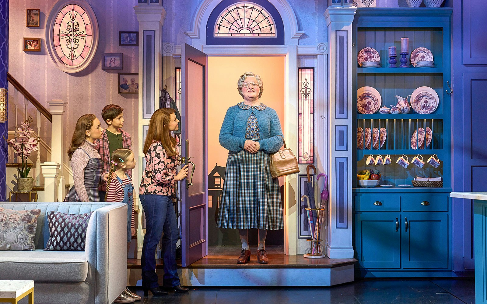 Family greeting Mrs. Doubtfire at the door in a cozy living room setting.