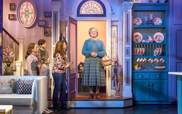 Family greeting Mrs. Doubtfire at the door in a cozy living room setting.
