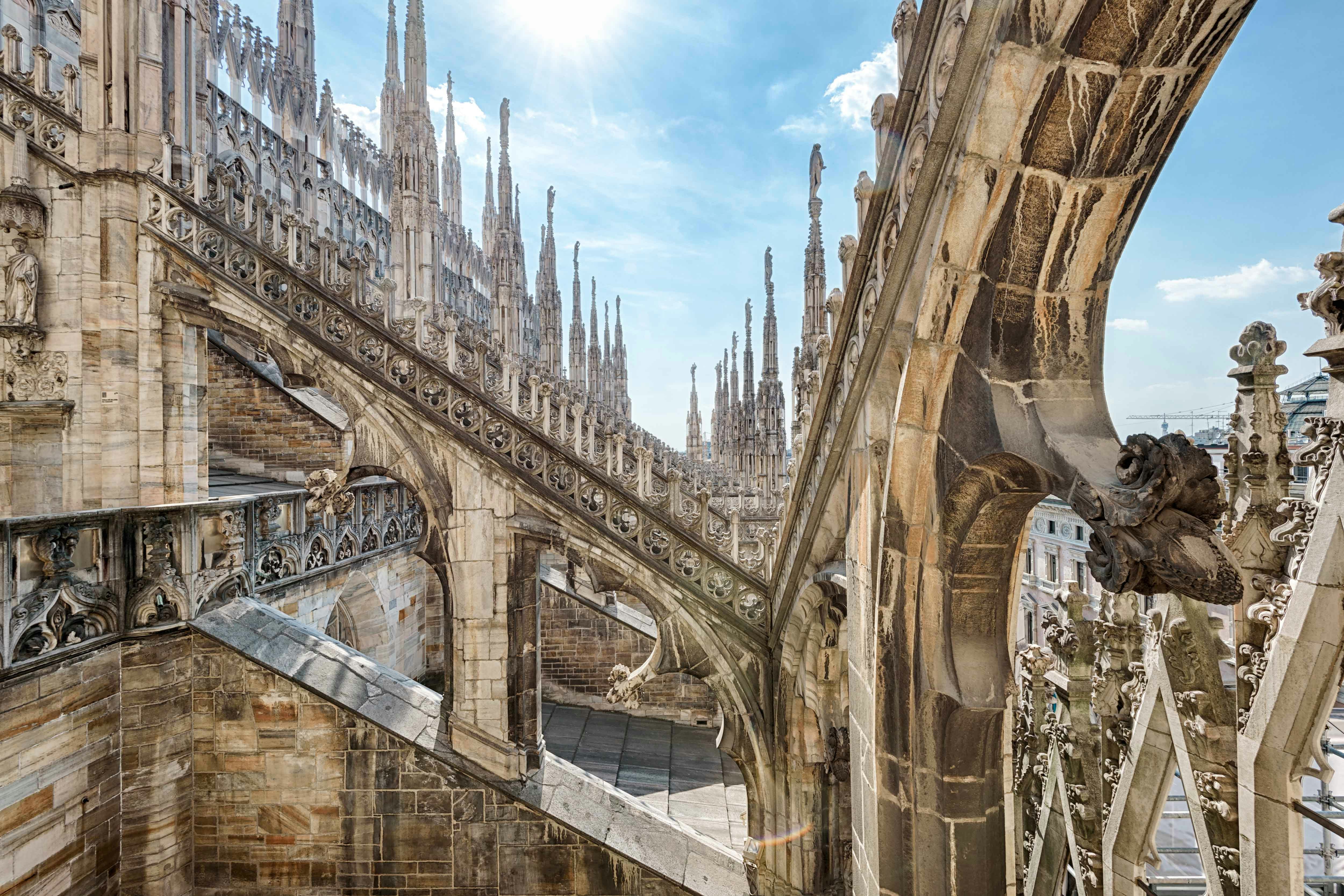 Duomo Milan rooftops with intricate spires and stone carvings under a clear sky.