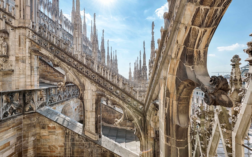 Duomo Milan rooftops with intricate spires and stone carvings under a clear sky.