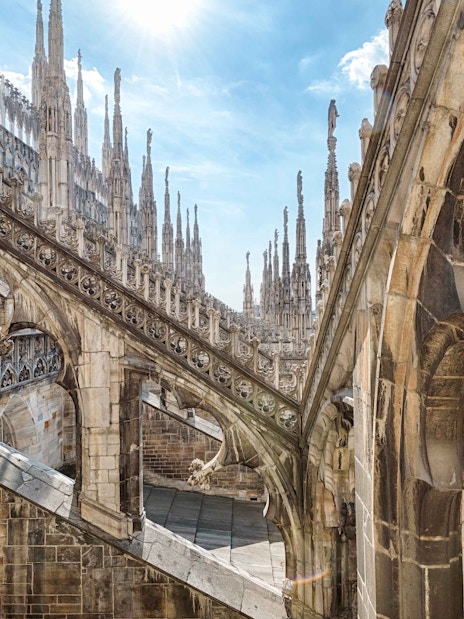 Duomo Milan rooftops with intricate spires and stone carvings under a clear sky.