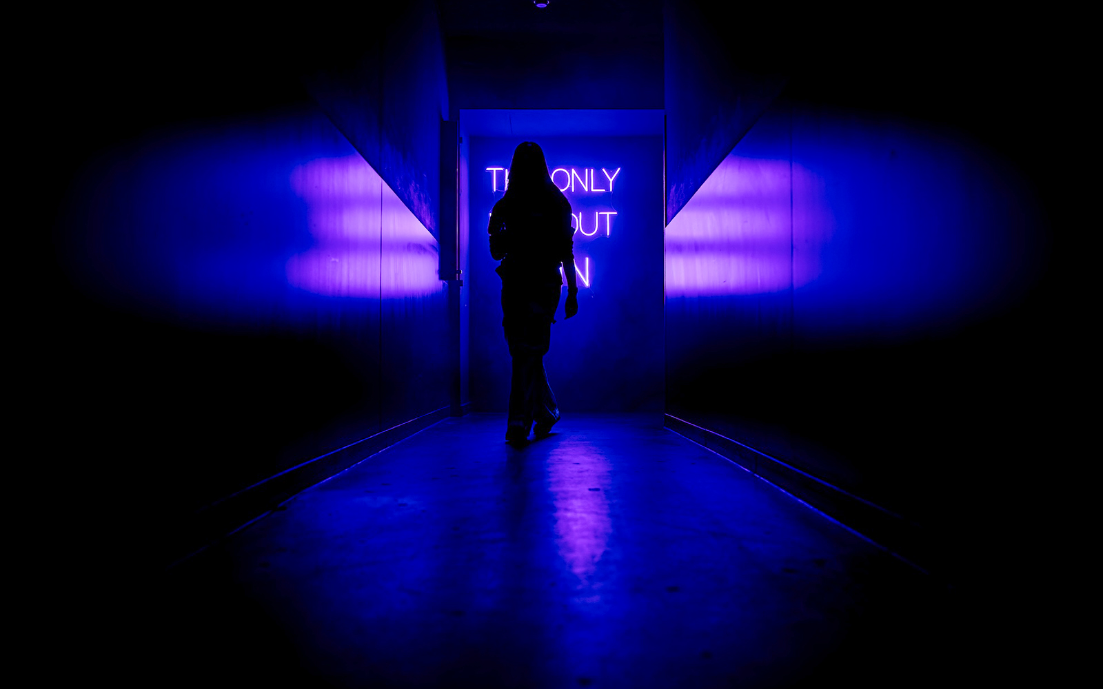 Silhouette walking towards neon sign inside Amaze Amsterdam.