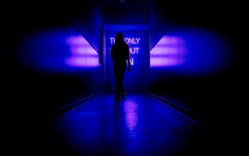 Silhouette walking towards neon sign inside Amaze Amsterdam.